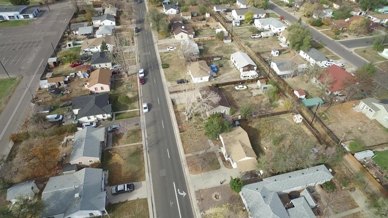 High aerial frame over Hidden Lake, Colorado homes, yards, parked cars, and a straight two-lane road, with no visible people.