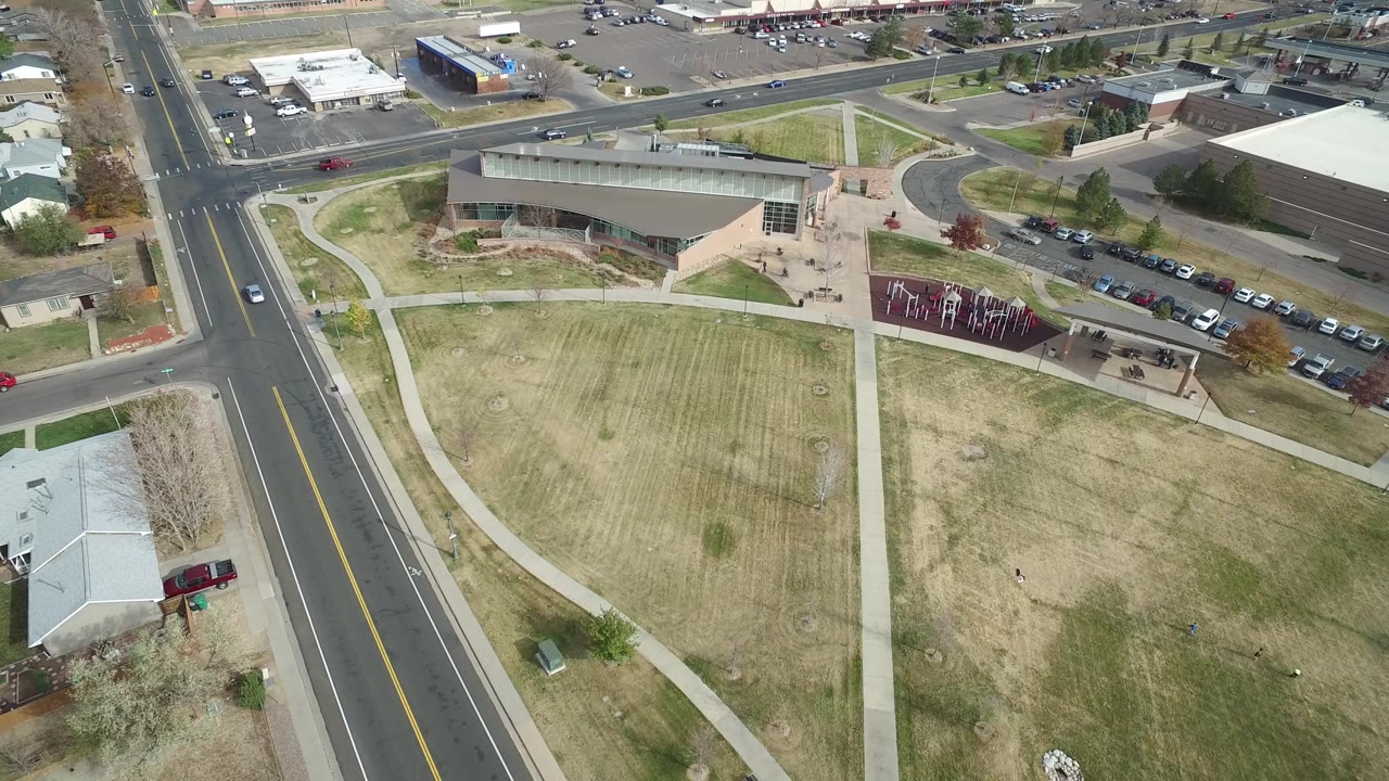 Aerial frame of a suburban block with buildings, cars, sidewalks, and grass.