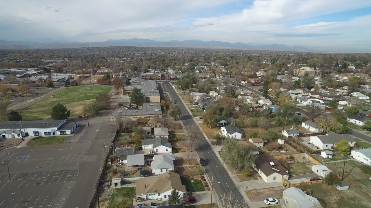 Aerial view of homes, road, parking lot, green field, and distant mountains.