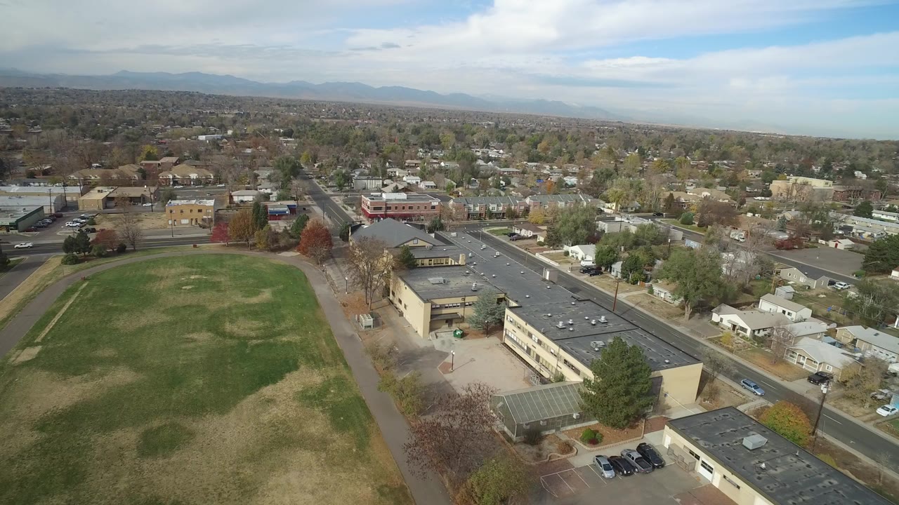 Aerial view of an oval green field beside low-rise buildings and suburban streets.