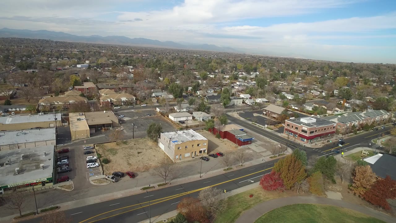 High aerial view over roads, low-rise buildings, homes, and distant mountains.