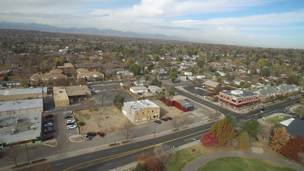 Hidden Lake, Colorado aerial frame with parking lots in the foreground, a red-trimmed low-rise building near the road, homes beyond, distant mountains, and no visible people.