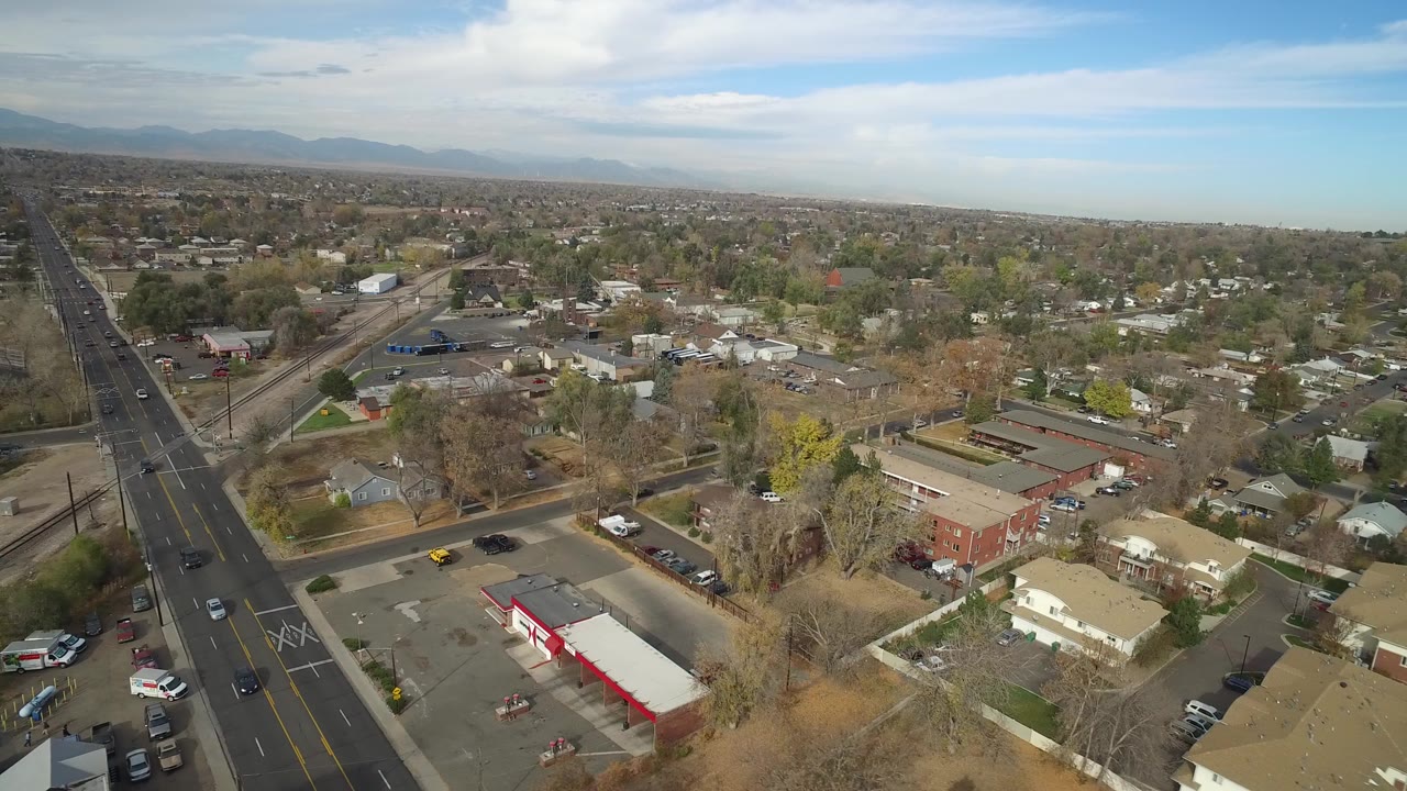 Aerial view over suburban streets, homes, rail tracks, and distant mountains.