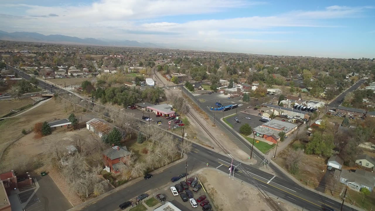 Aerial suburban landscape with a broad road, side streets, homes, trees, and commercial lots.