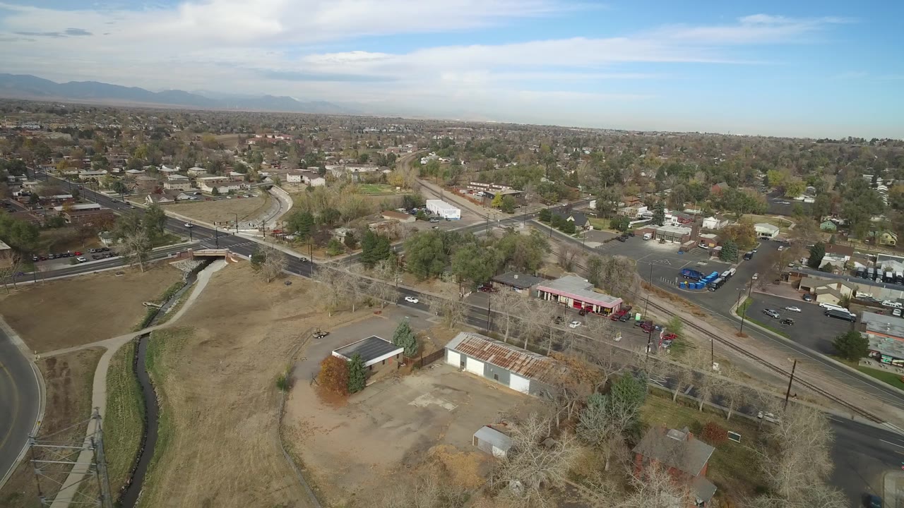 Drone view of a suburban intersection beside open land and low buildings.