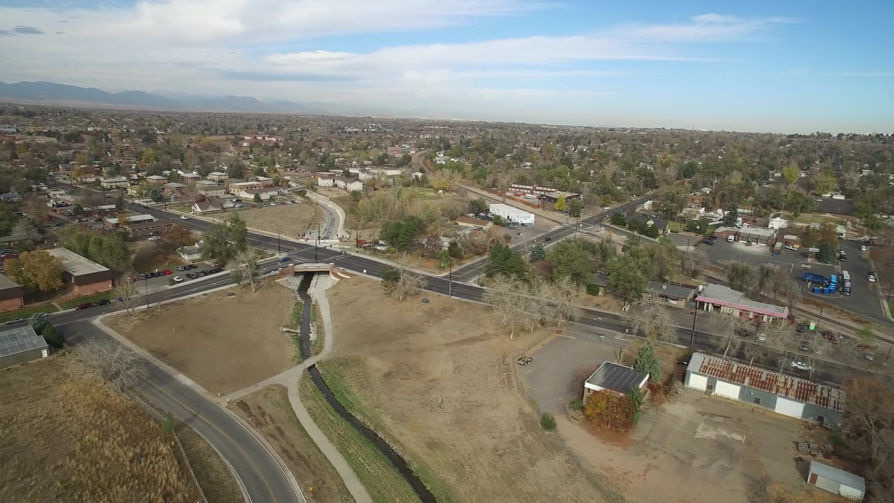 Aerial frame in Hidden Lake, Colorado with the bridge centered near road lanes, brown open ground, parked cars, low buildings, residential streets, and no visible people.