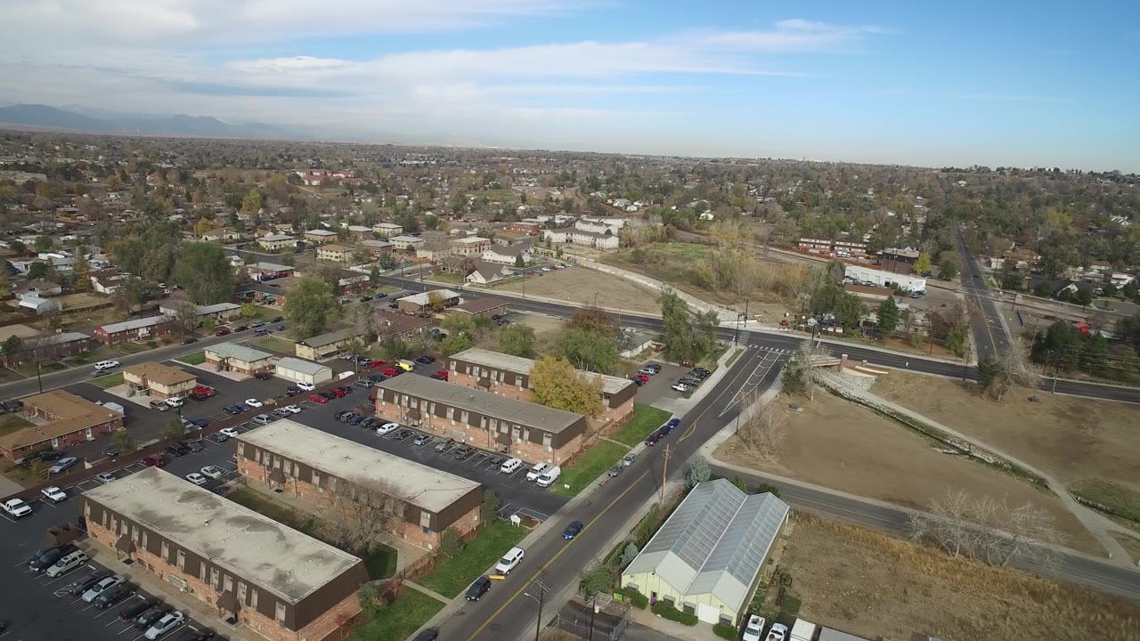Aerial view of low-rise buildings, roads, trees, and a flat town under blue sky.