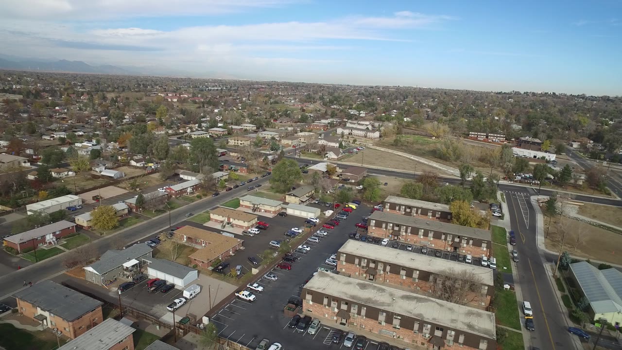 Aerial view over suburban buildings, parking lots, roads, and distant mountains.