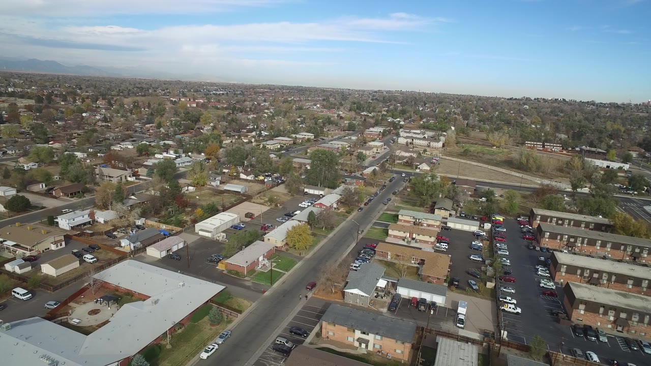 Aerial view over roads, apartments, houses, and parked cars under a blue sky.