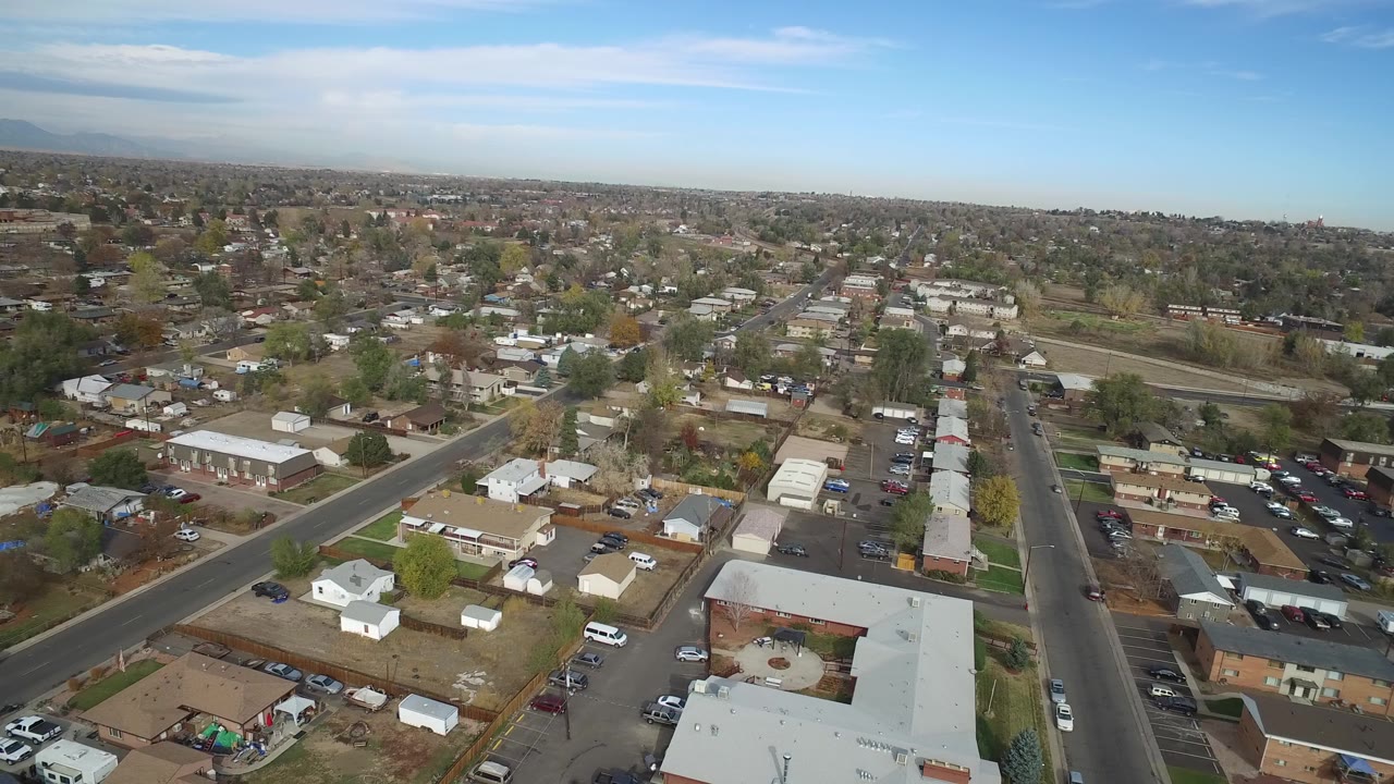 Aerial frame over Hidden Lake, Colorado showing houses, yards, parked cars, side streets, a main road, open lots, trees, and no clearly recognizable people.