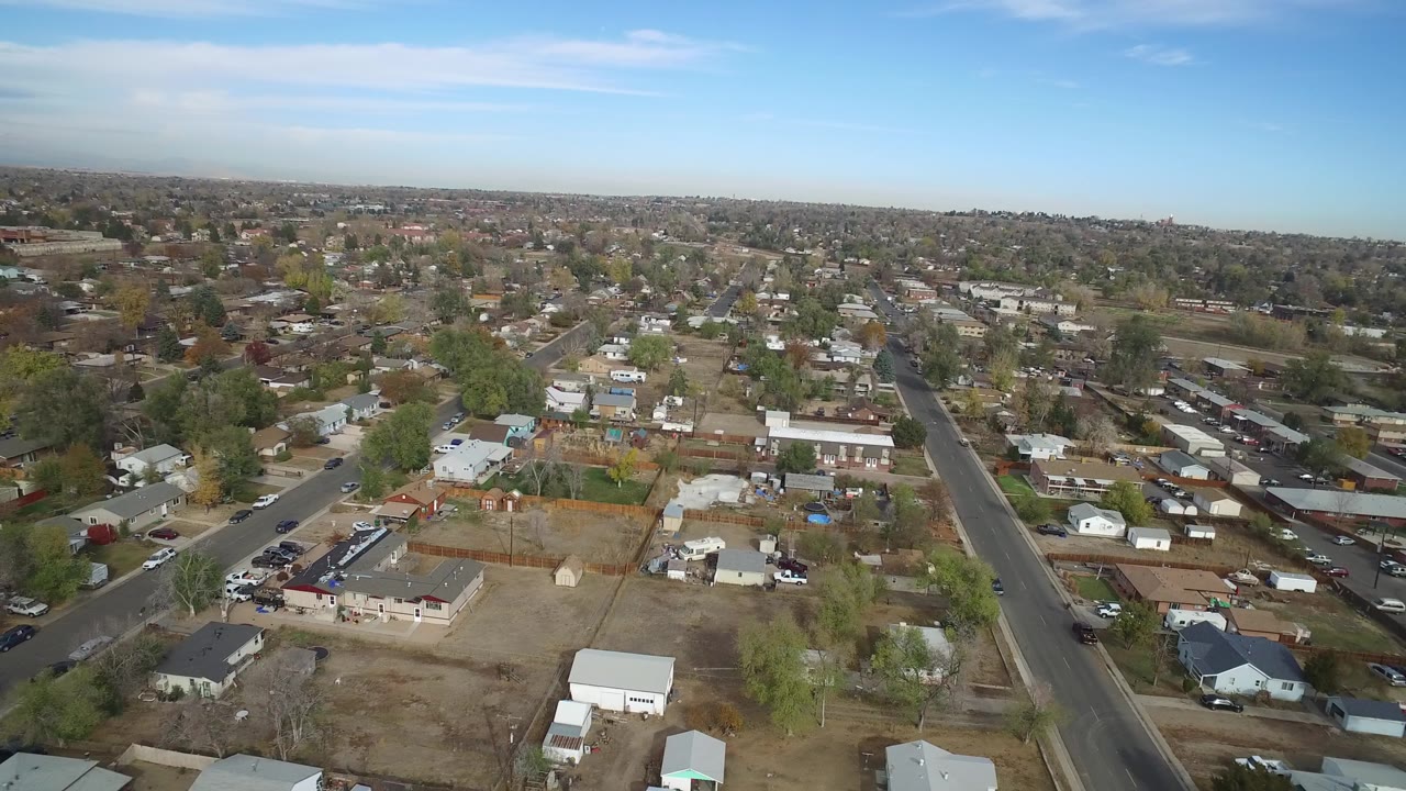 Opening aerial frame over Hidden Lake, Colorado shows residential streets, single-family houses, open lots, scattered trees, distant rooftops, and no visible people.
