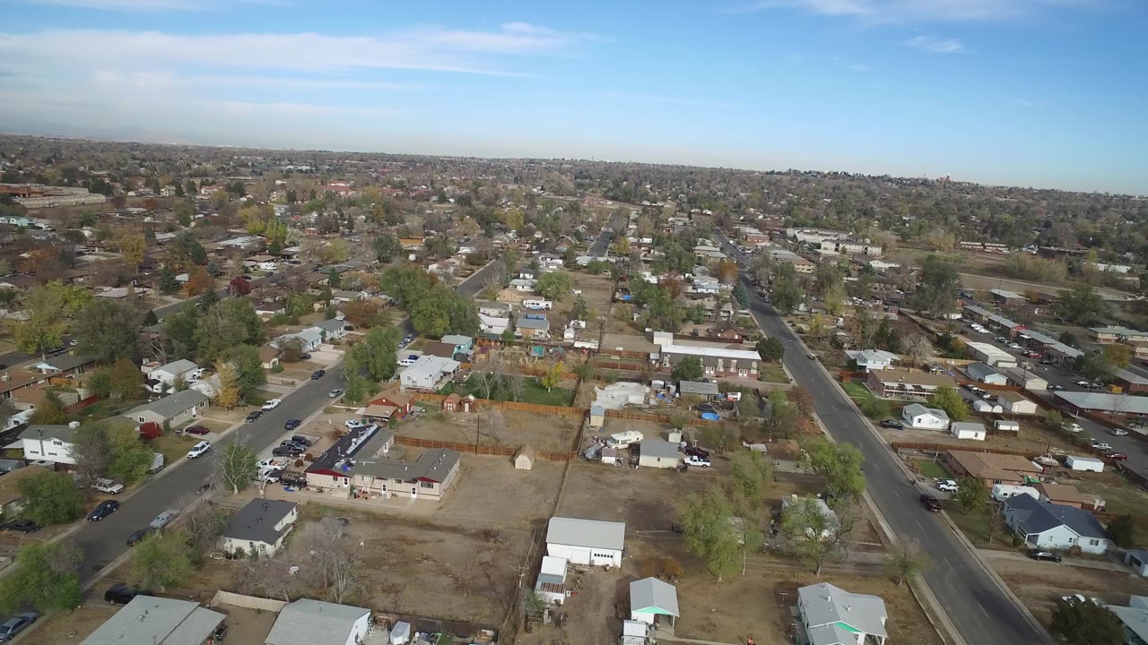 Drone-height view of a suburban neighborhood with roads, homes, lots, and trees.