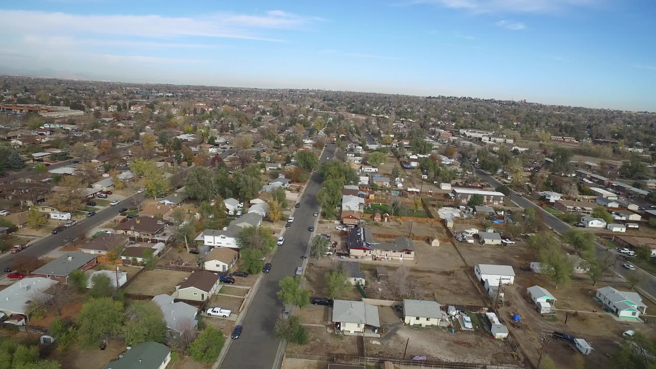 Aerial view of a residential neighborhood with roads, houses, trees, cars, and blue sky.