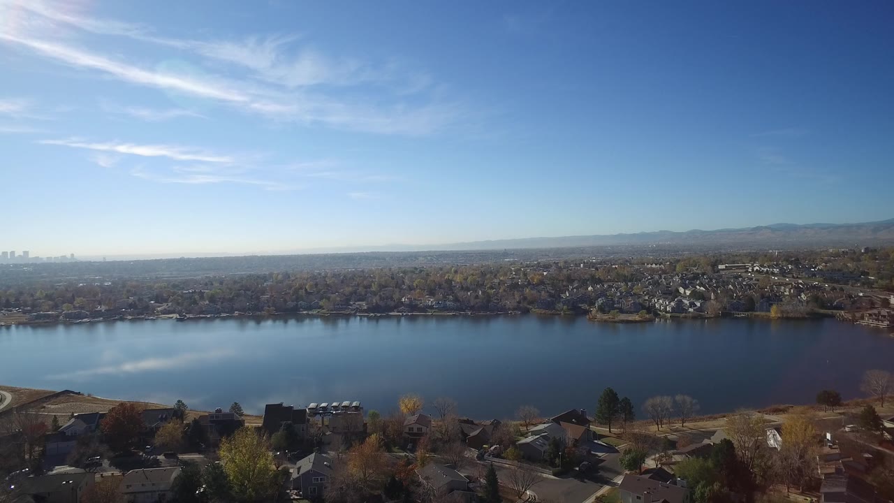 Blue lake bordered by trees and neighborhoods under clear daylight.