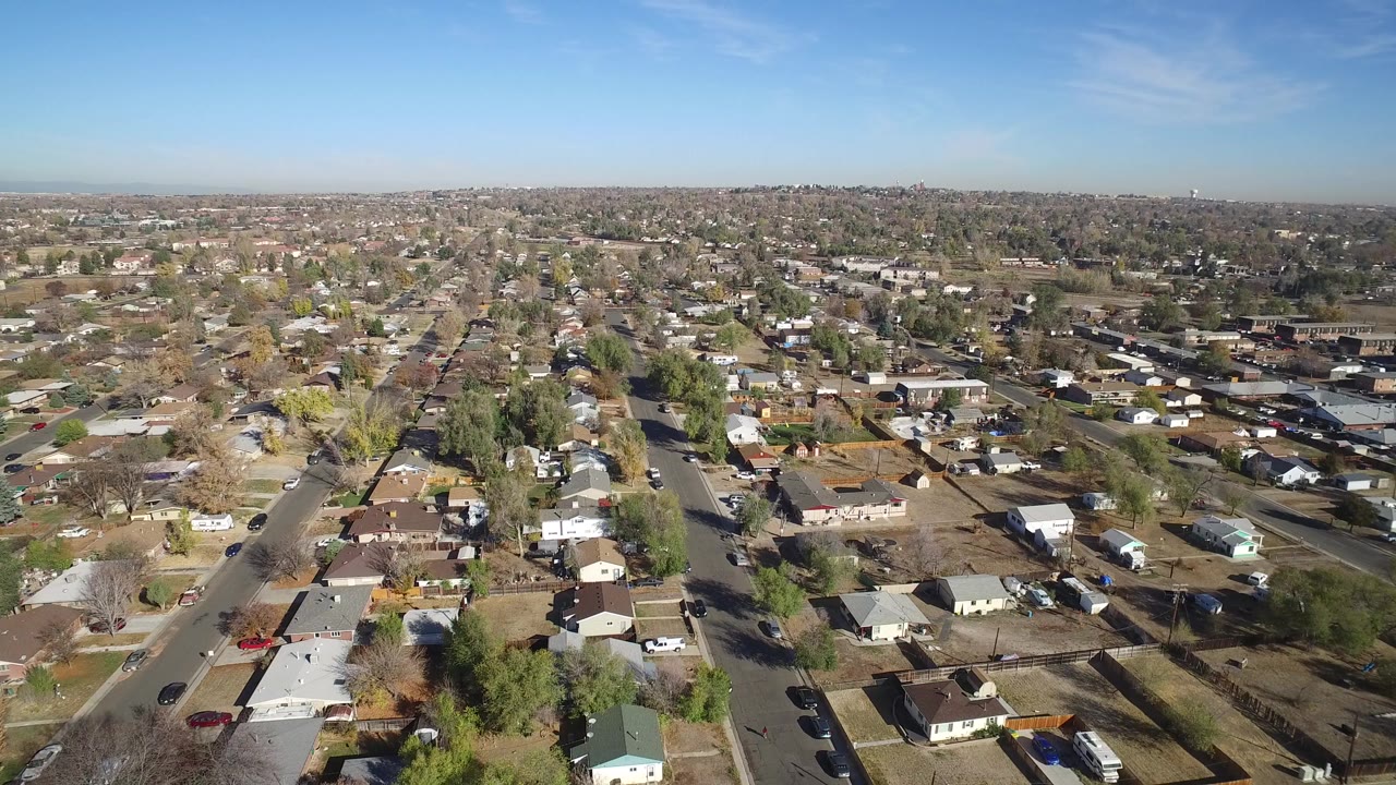 Aerial view over suburban houses and roads under clear daylight.