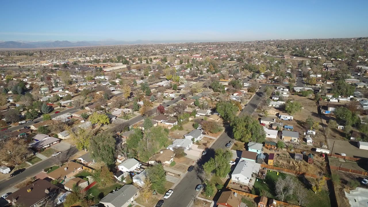 High aerial view over Hidden Lake, Colorado homes, streets, yards, parked cars, and distant mountains, with no clearly visible people in this frame.