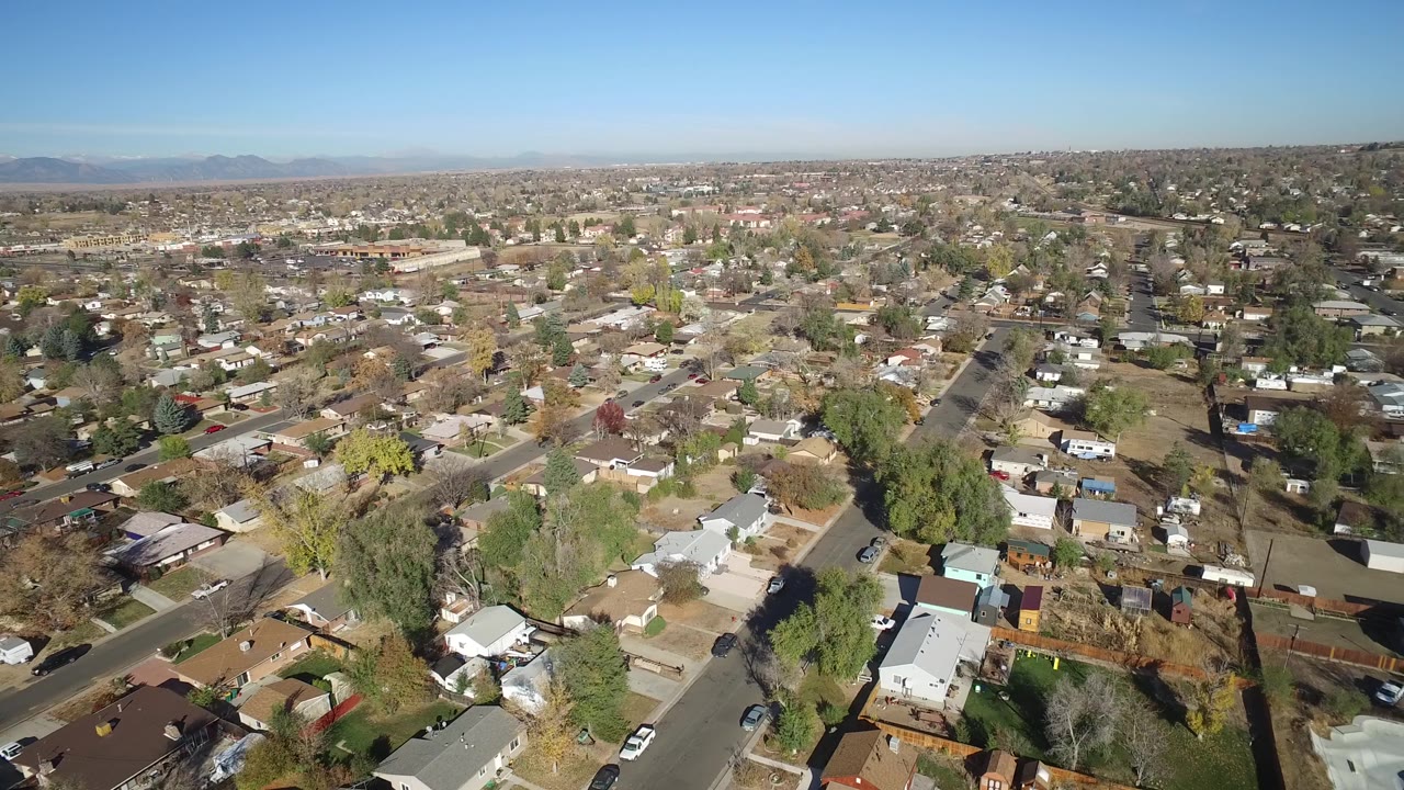 Elevated Hidden Lake, Colorado view showing rooftops, fenced backyards, parked vehicles, mature trees, and a long residential grid under clear daylight.
