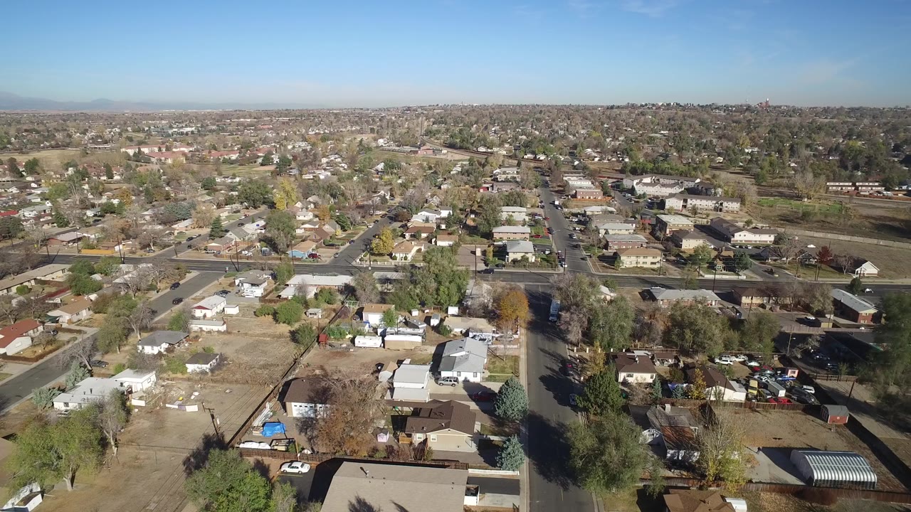 Aerial view of suburban homes, roads, trees, and clear blue sky.