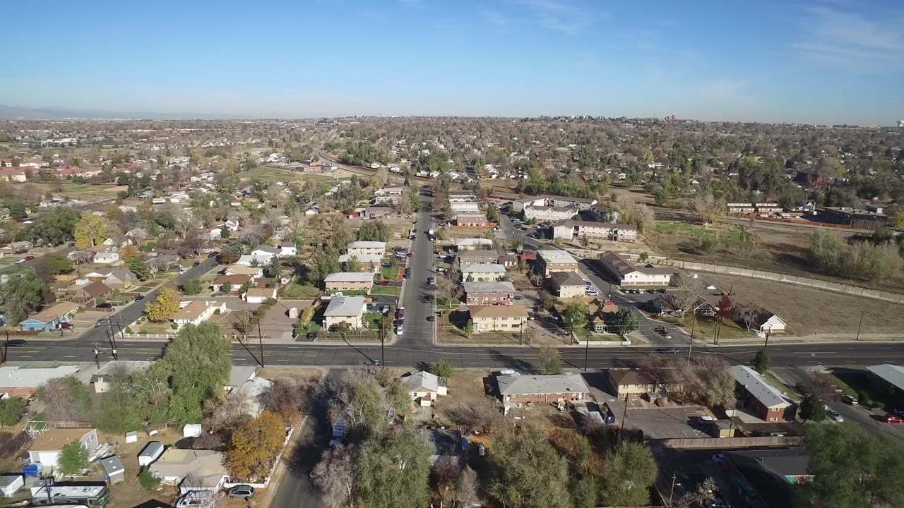 Aerial view of suburban homes and a broad road under blue sky.