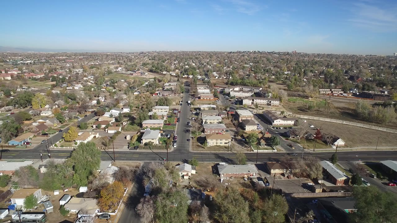 Hidden Lake, Colorado aerial frame centers a straight residential street running away from the camera, with cars, low buildings, bare trees, and no visible people.