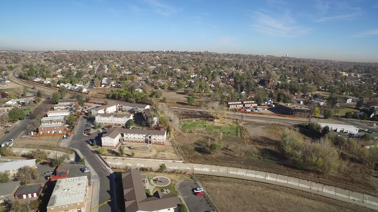 High drone view over Hidden Lake, Colorado with apartment buildings in the foreground, roads and open ground through the middle, a tree-filled residential horizon, and no visible people.