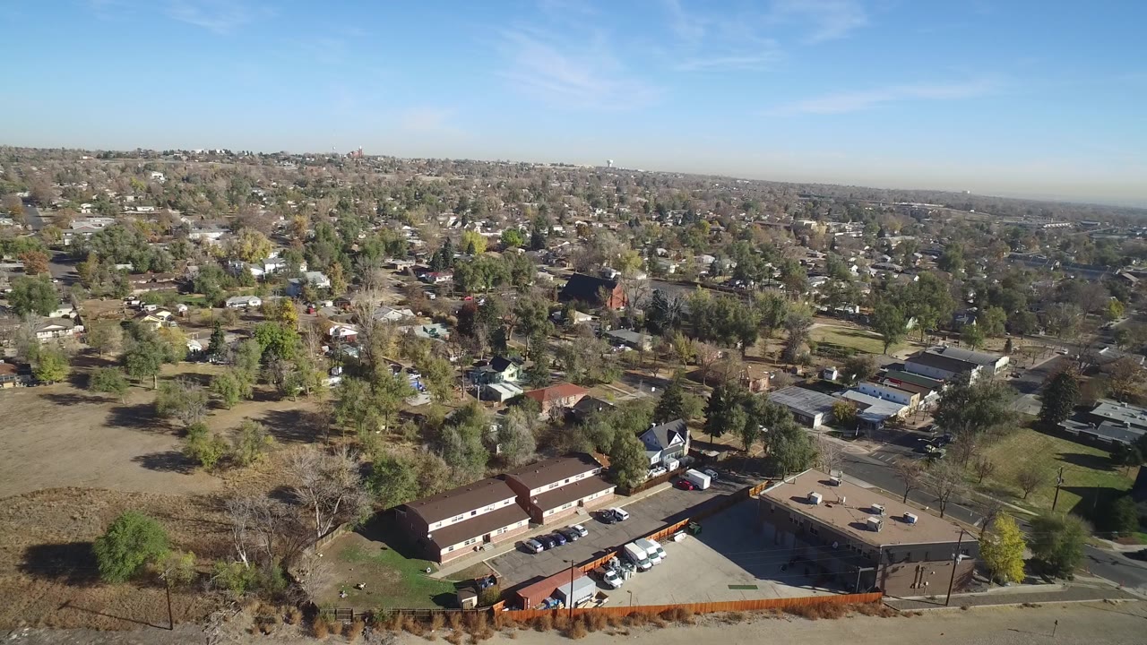 Drone-style view of houses, trees, roads, and low buildings in daylight.
