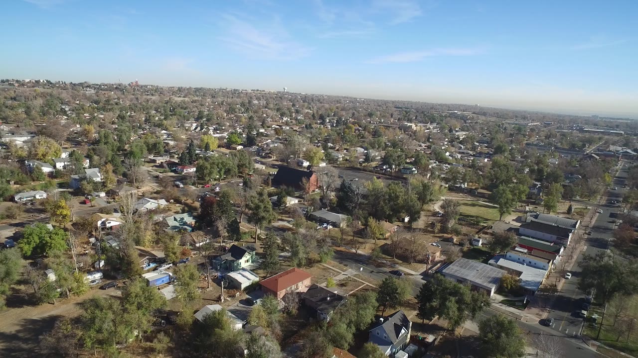 Aerial view over a residential neighborhood with houses, trees, streets, and blue sky.