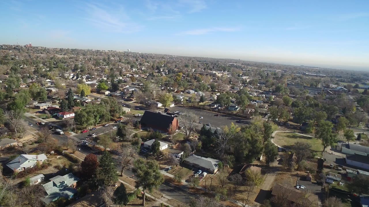 Wide aerial view over houses, trees, roads, and a clear blue sky.