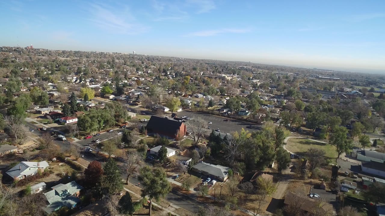 Aerial frame over Hidden Lake, Colorado, with the dark-roofed building more central, surrounding homes, parked cars, bare trees, and no visible people.