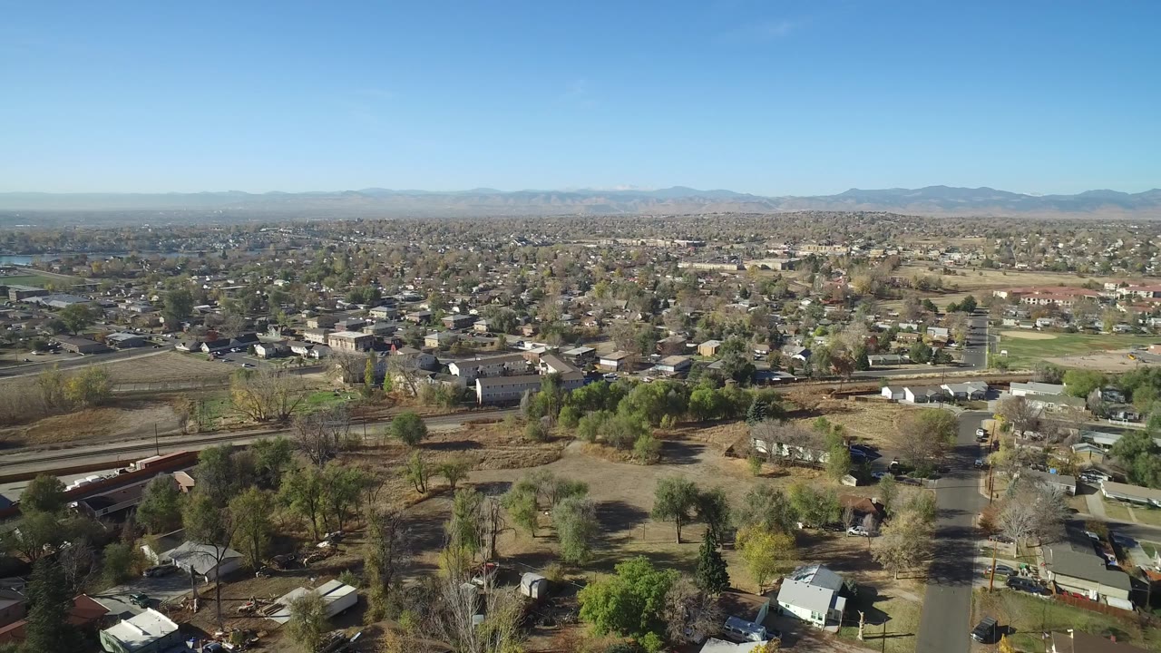 Wide aerial view of houses, open lots, trees, roads, and mountain backdrop.
