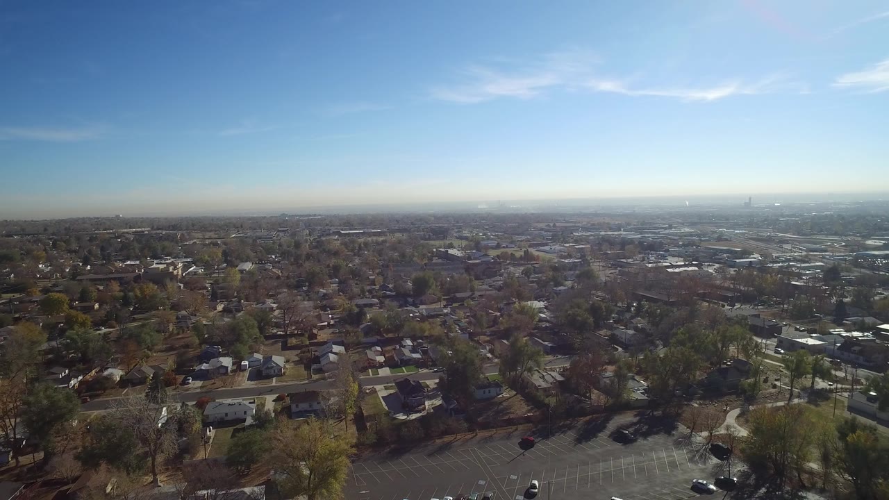 High aerial view over suburban homes, trees, roads, and a hazy city horizon.