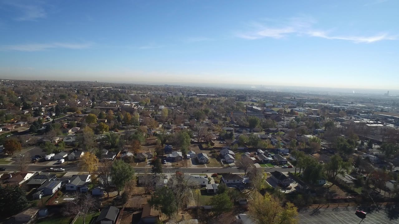 Wide aerial view over suburban houses and tree-lined streets under blue sky.