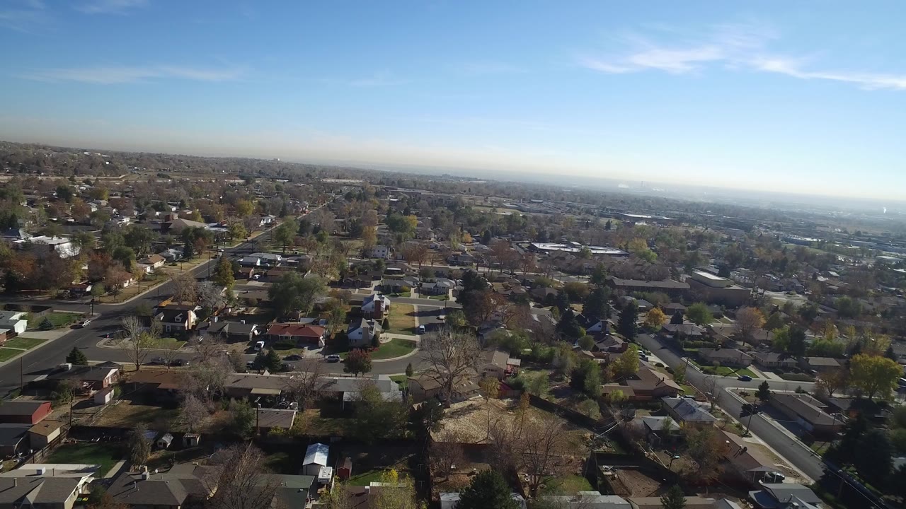 Aerial view over suburban houses and tree-lined streets under blue sky.