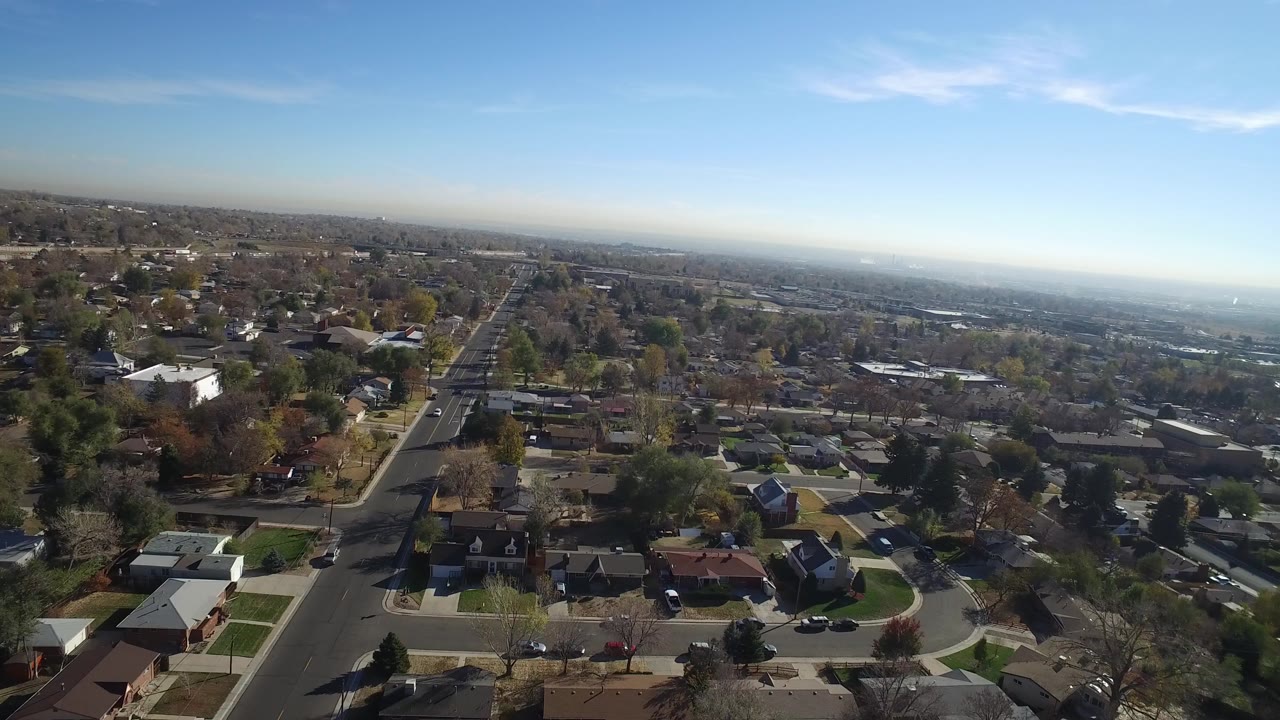 Opening aerial frame over Hidden Lake, Colorado with a long straight road, low houses, scattered trees, a hazy distant horizon, and no visible people.