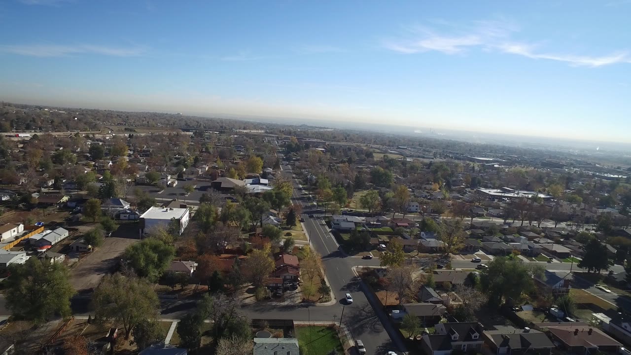 Aerial frame over Hidden Lake, Colorado with residential streets, low houses, scattered trees, blue sky, distant haze, and no visible people.