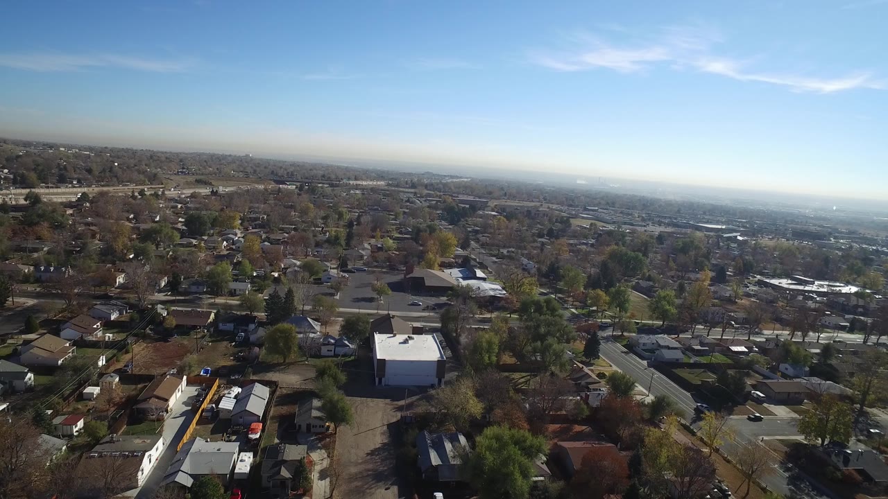 High aerial view over a residential town with roads, trees, rooftops, and blue sky.