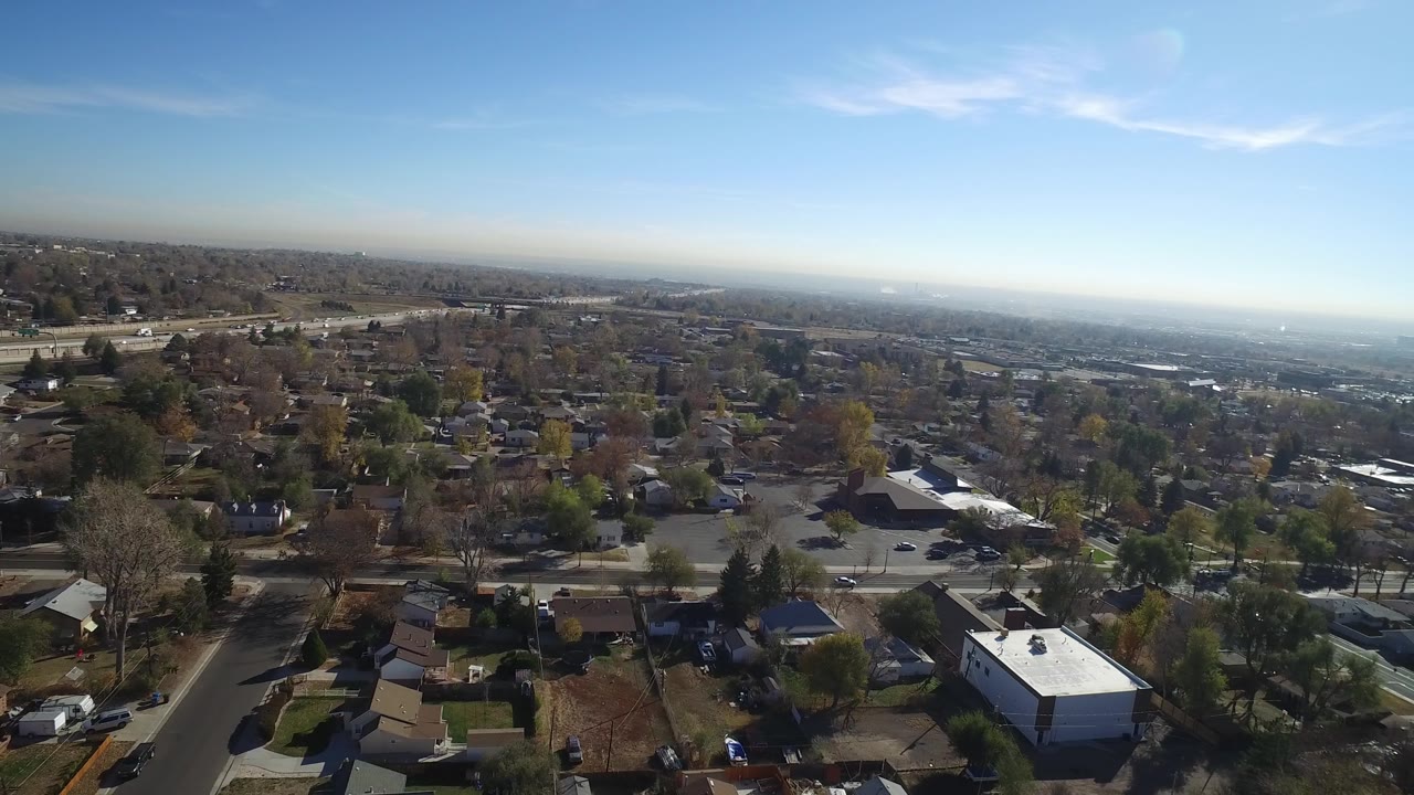 Aerial frame over Hidden Lake, Colorado, with a broad neighborhood foreground, the highway running across the left side, distant haze, and no visible people.