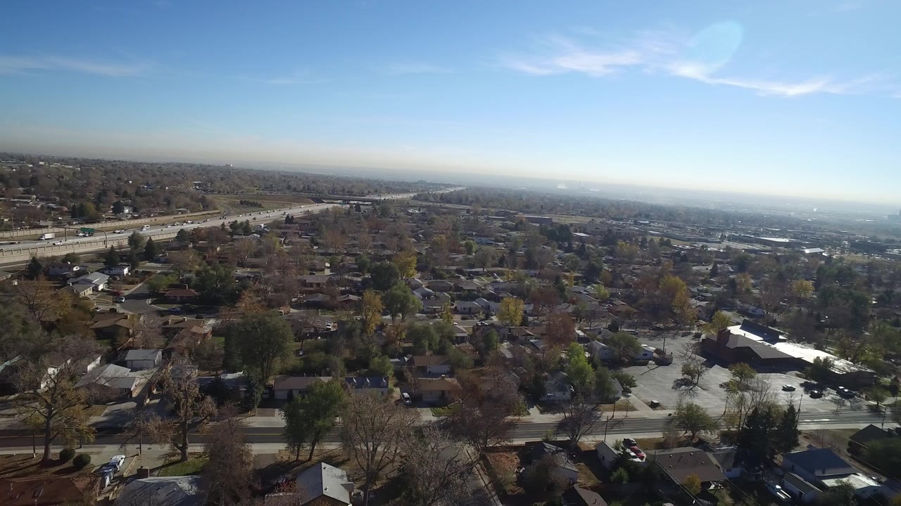 Aerial view over homes, trees, roadway, and blue sky.