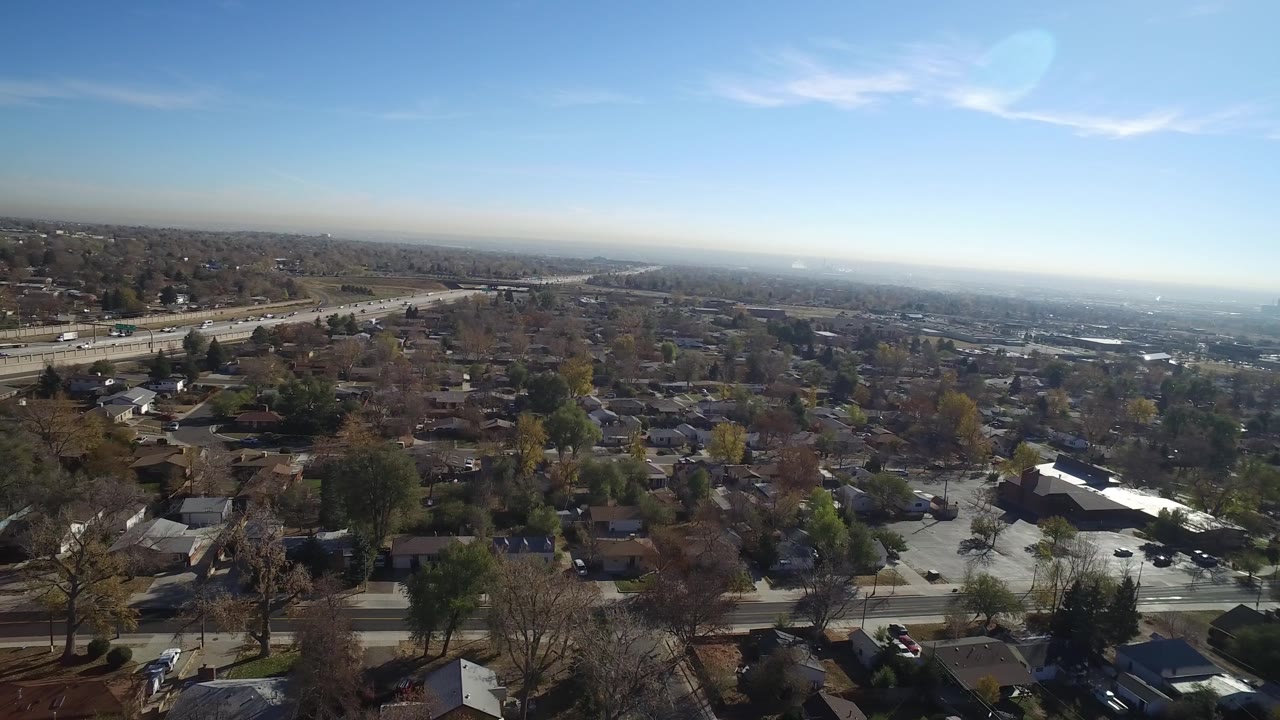 Aerial view across Hidden Lake, Colorado showing houses and leafless trees below, a road corridor on the left, haze near the horizon, and no visible people.
