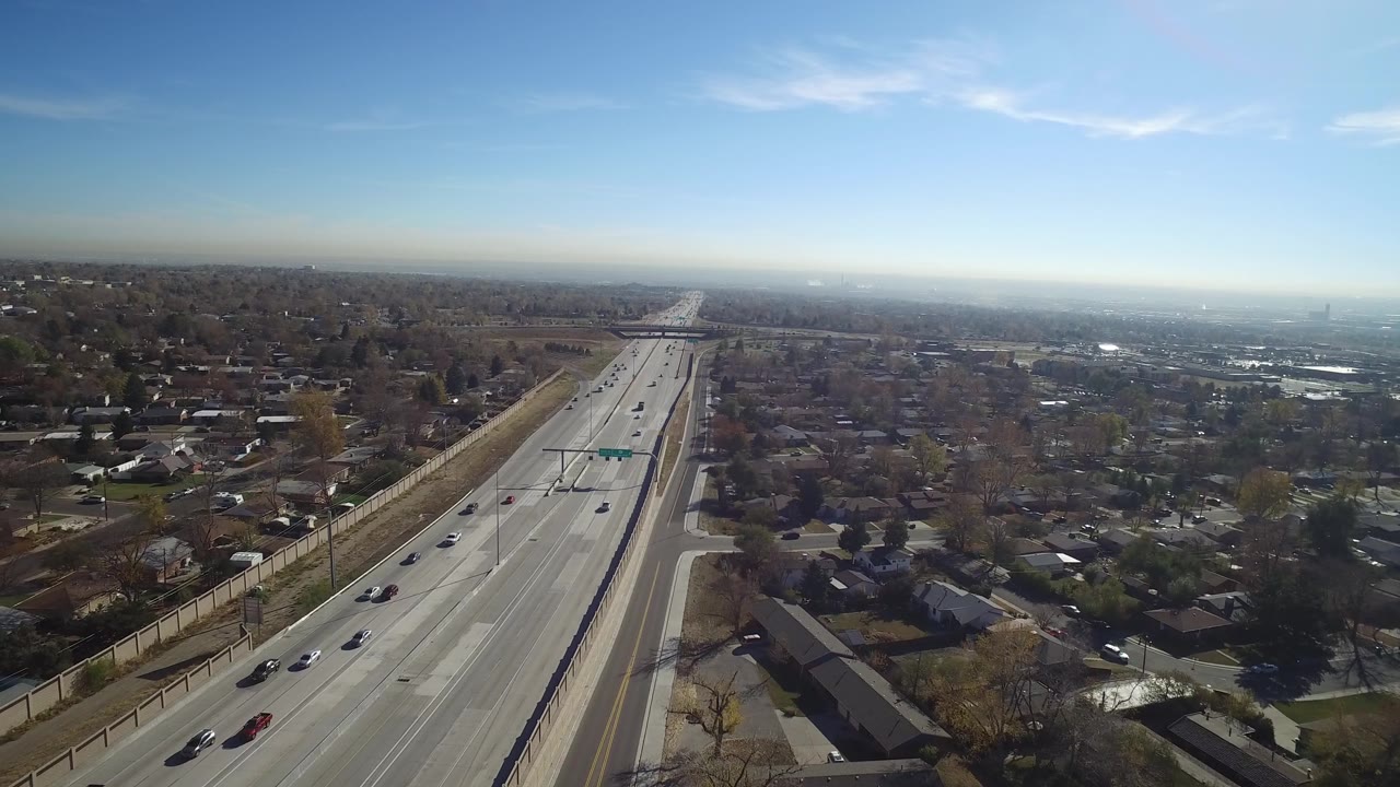 Wide drone-like view of a straight road running toward the horizon through suburbs.