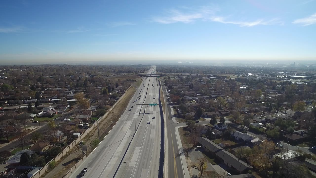 Opening aerial frame of a wide road in Hidden Lake, Colorado, with cars on both sides, houses and trees beside the roadway, and no visible people.