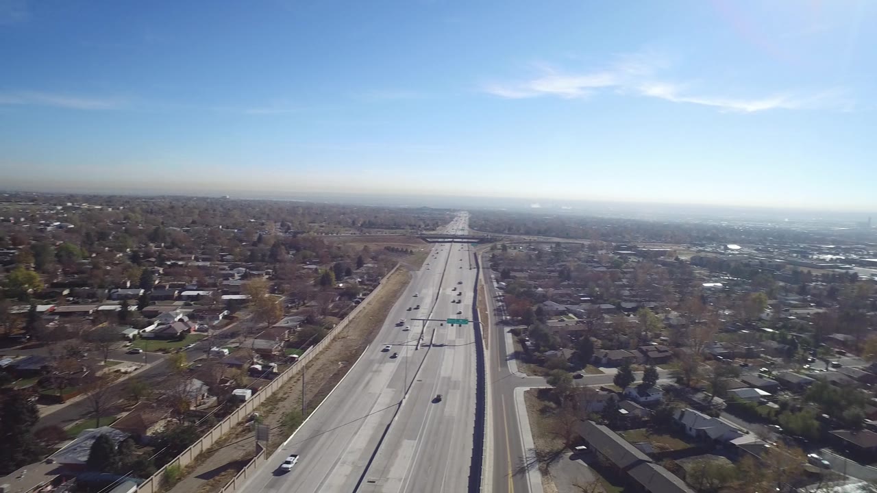 A wide Hidden Lake, Colorado aerial shows light traffic on the highway, clustered homes, bare and evergreen trees, a hazy distance, and no visible people.