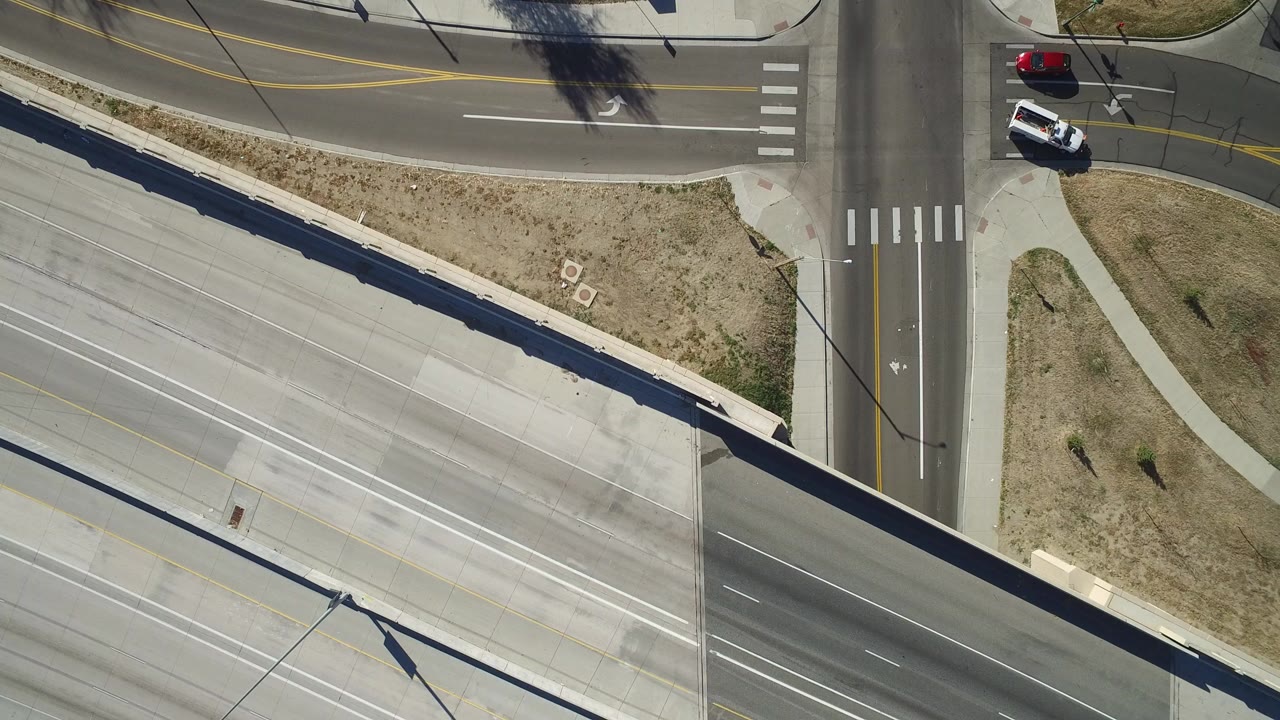 Overhead view of a bridge crossing a suburban intersection with cars near the crosswalks.