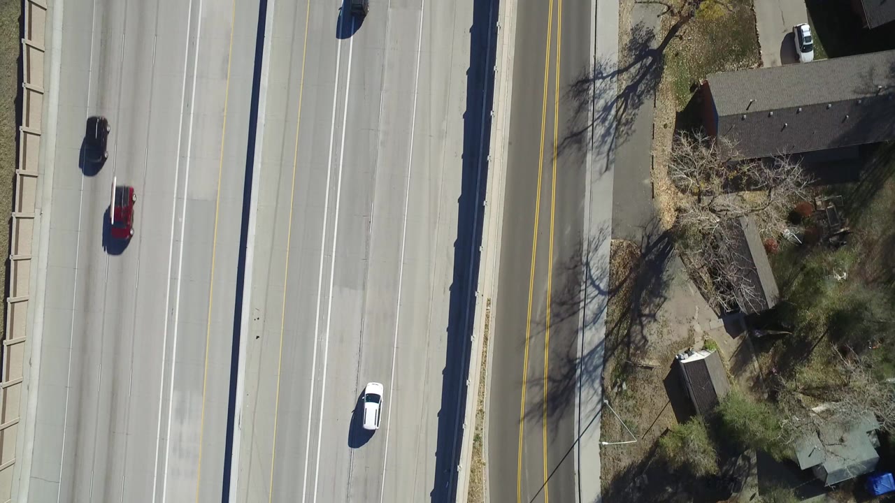 Aerial frame over Hidden Lake, Colorado, showing cars spaced across highway lanes, a parallel two-lane road, houses, winter-bare trees, and no visible people.