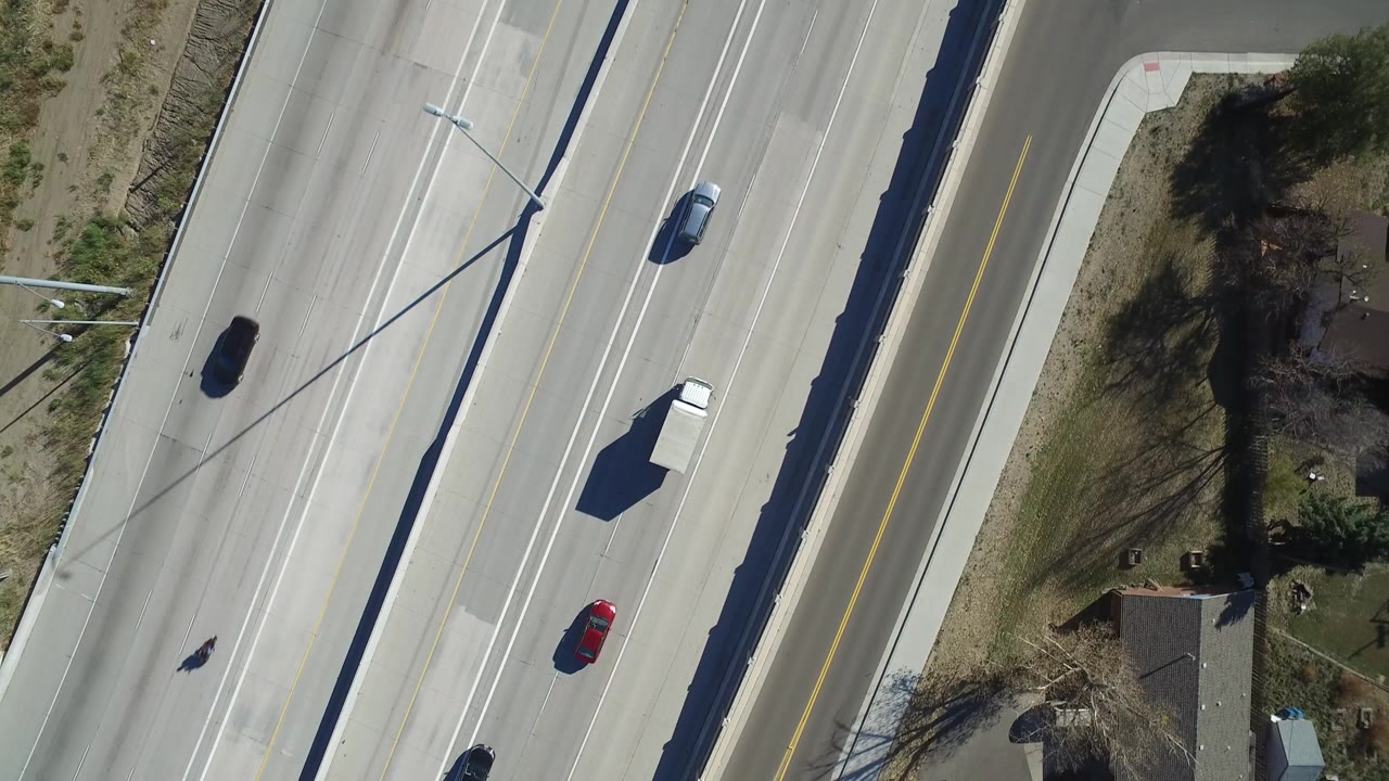 Overhead highway lanes with cars, a white truck, streetlight shadows, and homes near the road.