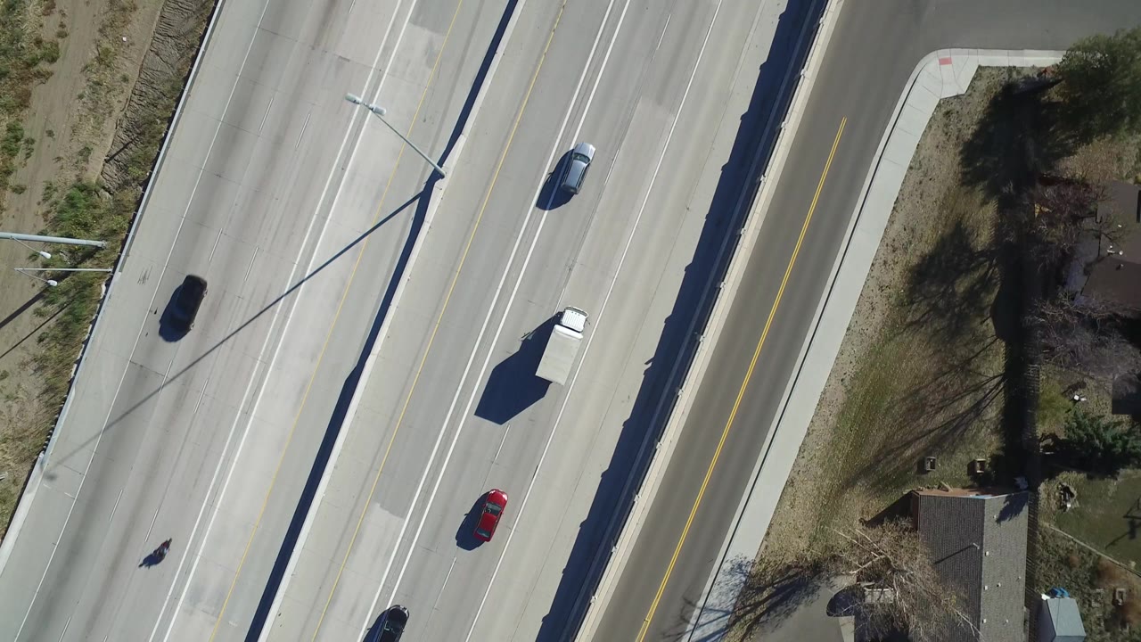 Overhead frame of Hidden Lake highway traffic with a white truck near the center lanes, a red car below it, dark vehicles in adjacent lanes, a house lot at right, and no visible people.