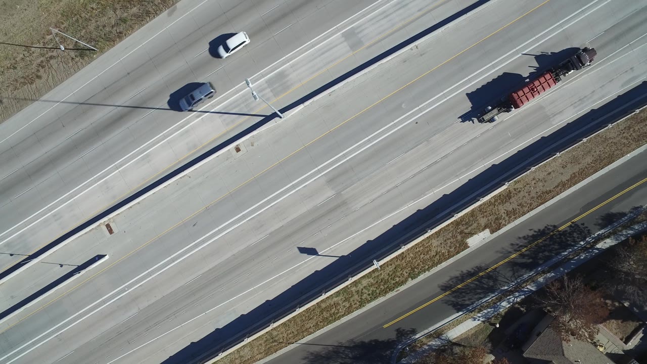 Aerial daylight frame in Hidden Lake, Colorado with cars moving along separated lanes, a long median edge, roadside grass strips, and no visible people.