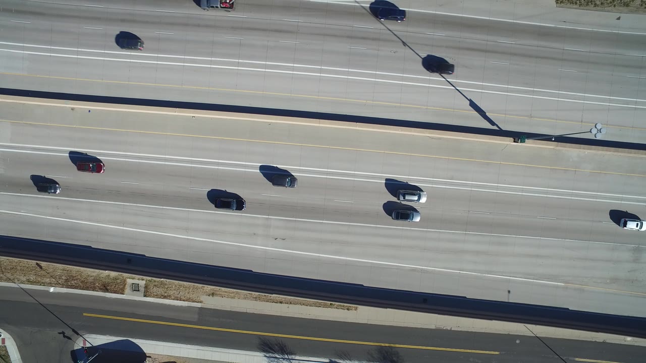 Top-down view of several cars and SUVs spaced across parallel highway lanes in Hidden Lake, Colorado, with a frontage road and grass edge visible below.