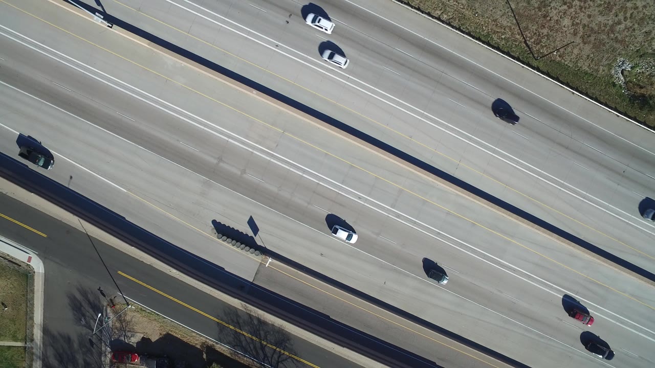 Overhead highway lanes with scattered cars and roadside grass.