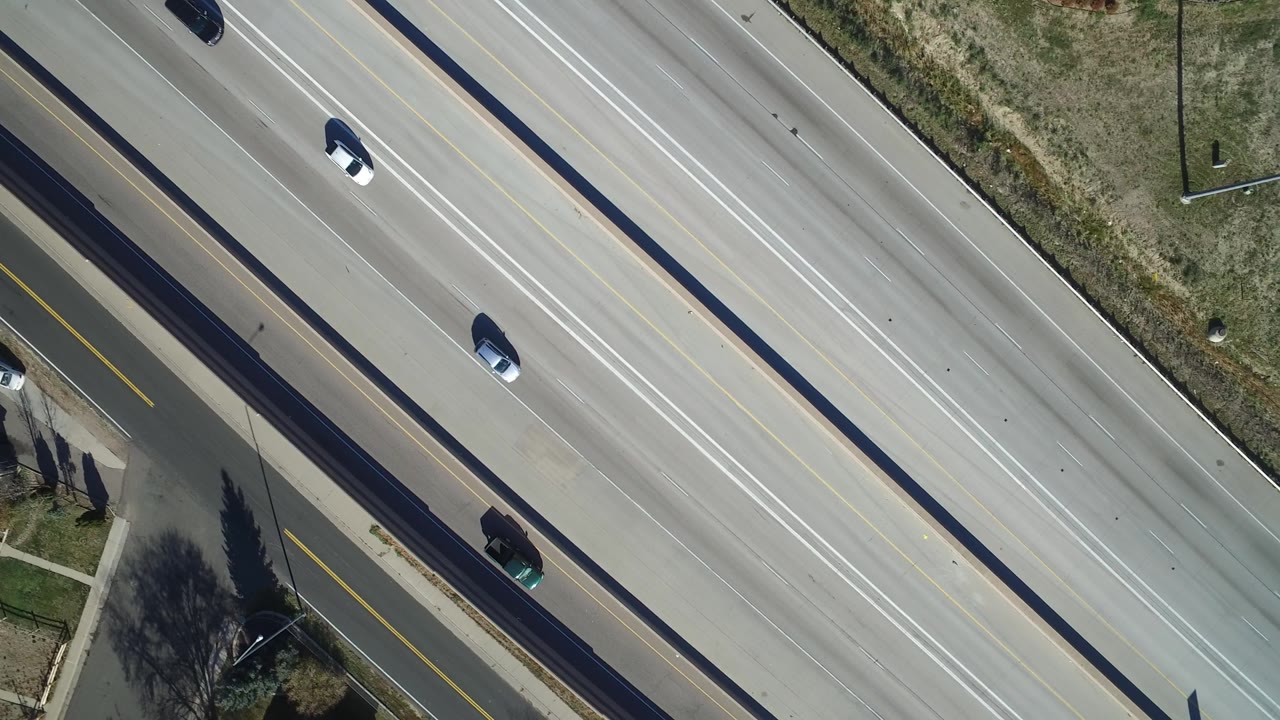 Aerial frame in Hidden Lake, Colorado showing cars separated across wide highway lanes, grassy roadside strips, a narrow side road, and no visible people.